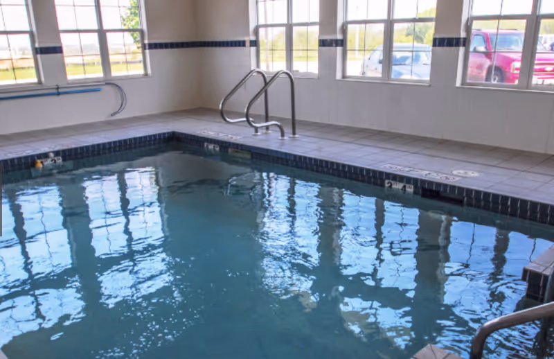 Indoor swimming pool with tiled deck, metal handrails and large windows showing parked cars outside.