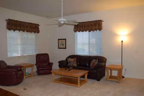 A comfortable living room with leather sofas, chairs, a coffee table, lamps, and windows.