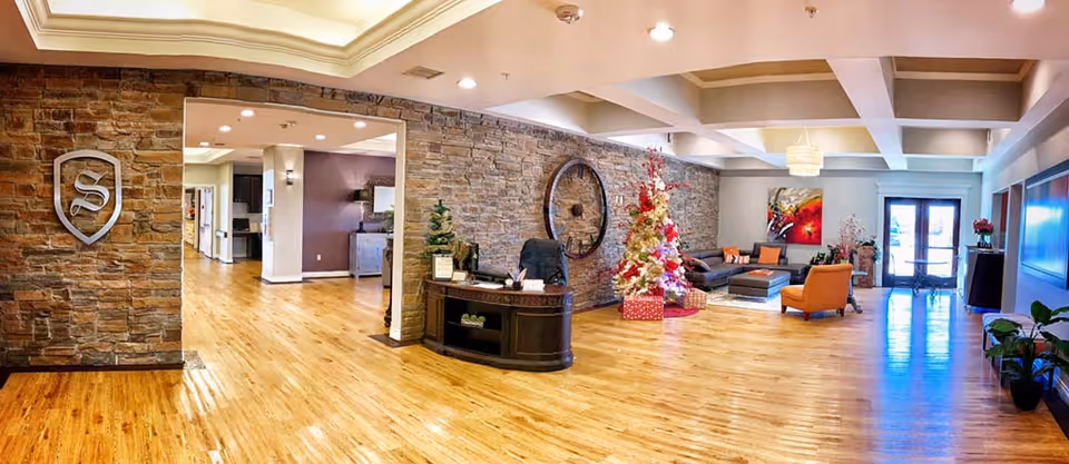 Spacious furnished lobby with hardwood floors, stone accent wall, reception desk, seating area, and decorated Christmas tree.