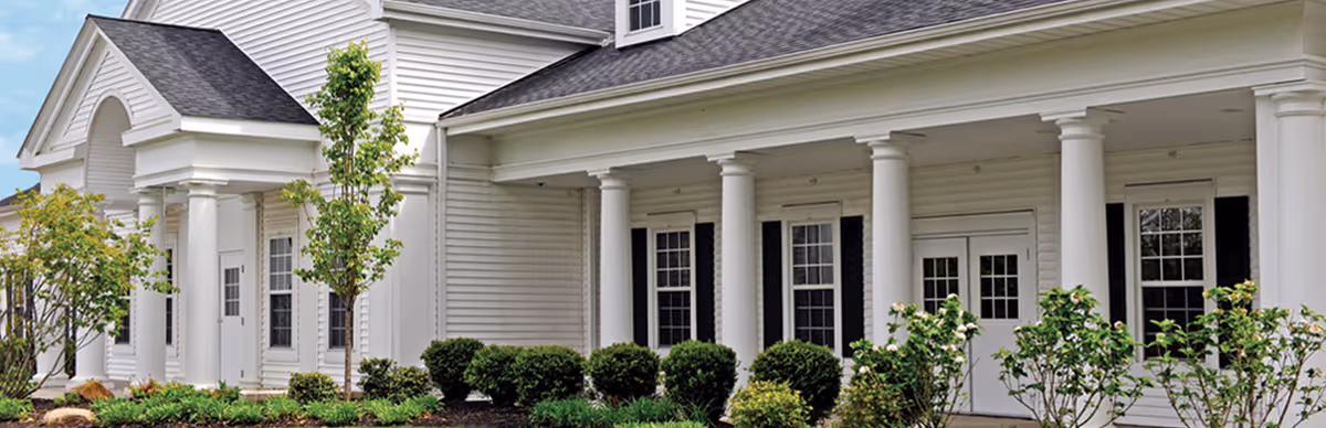 Front exterior of Rae-Ann Geneva senior living community, a white, columned building with a landscaped entrance.