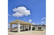 Entrance canopy and drive-up portico of a single-story nursing and rehabilitation building under a bright blue sky with scattered clouds.