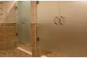 Interior view of a bathroom featuring a tiled floor and walls with a glass shower door and a white cabinet with silver handles.