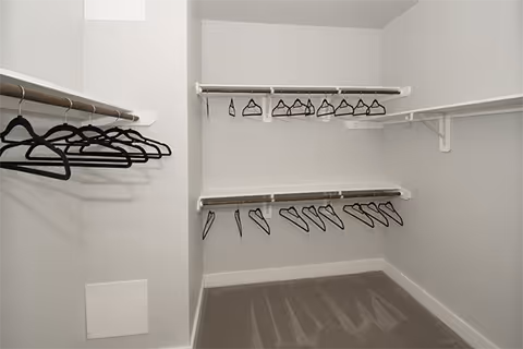 Empty walk-in closet with multiple hanging rods and black hangers.