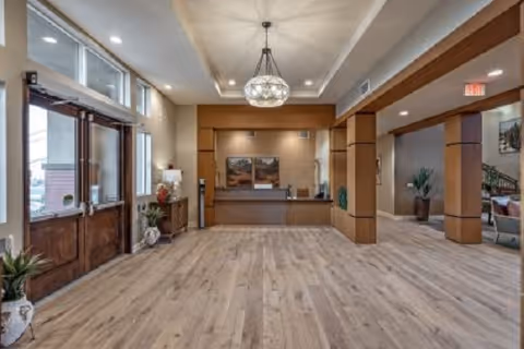 Spacious senior living lobby with a reception desk, wood flooring, seating area, and large windows at the entrance.