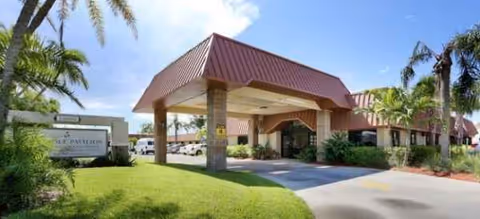 Exterior view of a senior living facility entrance with a covered drop-off and palm trees