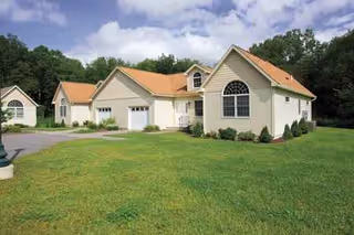 Single-story senior living building with beige siding and orange roofs, surrounded by green lawn.