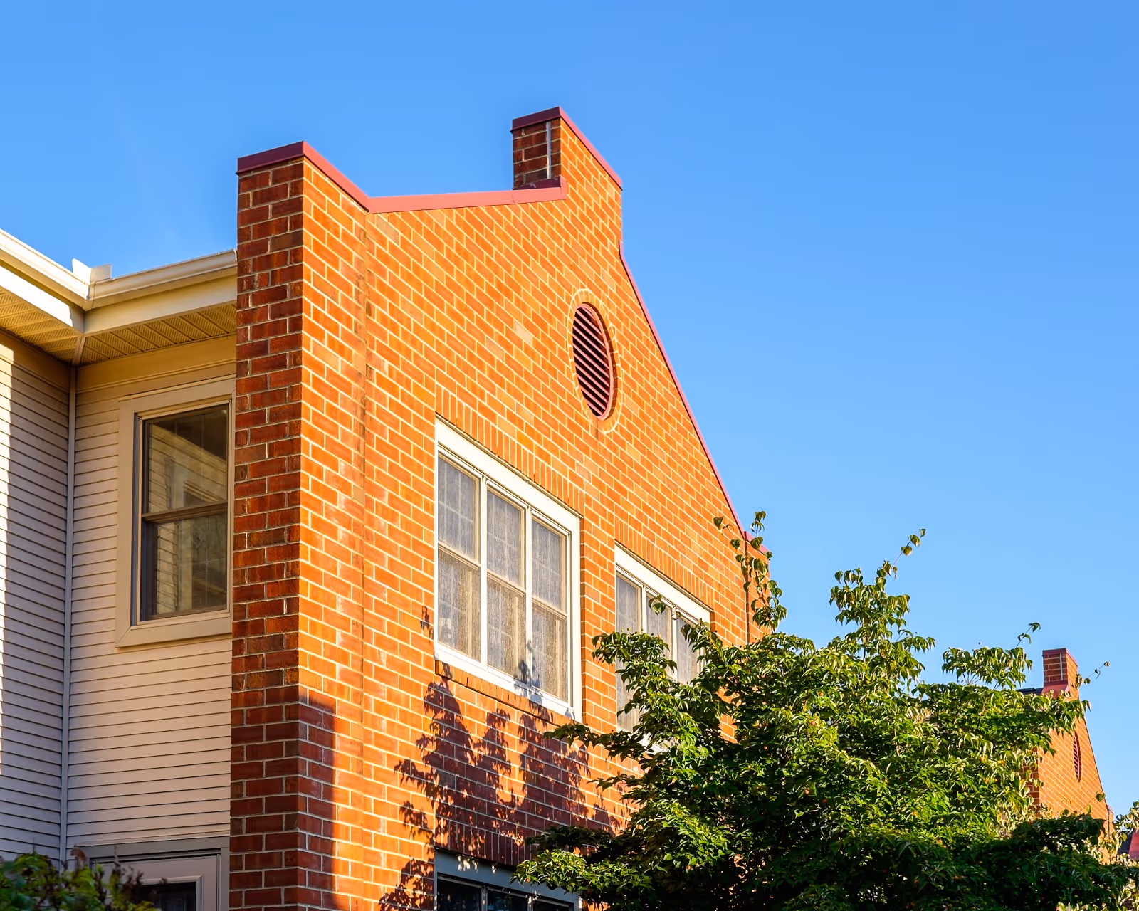 Exterior view of a brick and siding building under a clear blue sky with green trees in front.