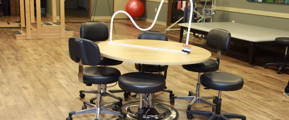 Round wooden table with black rolling chairs in a spacious interior activity room.