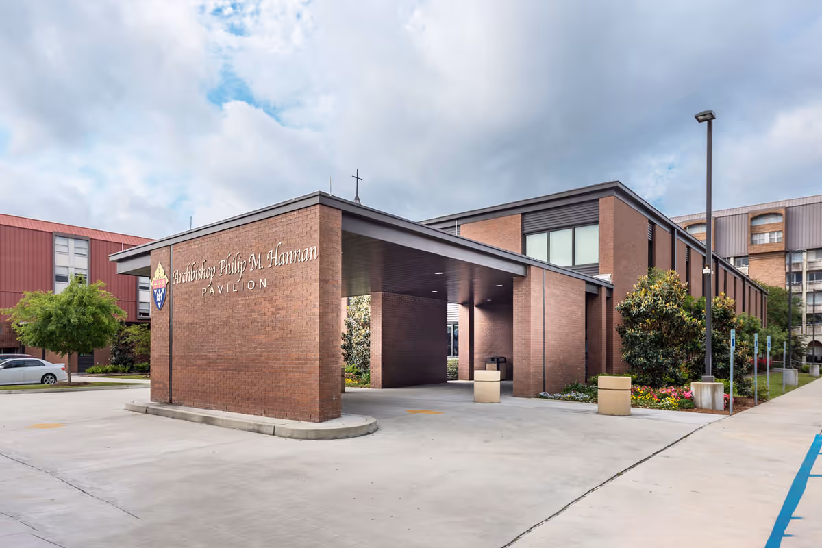 Drive-through entrance canopy of a brick pavilion building with signage reading 'Archbishop Philip M. Hannan Pavilion' and surrounding landscaping.