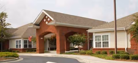 Brick-and-stone senior living facility entrance with a covered porte-cochere and manicured shrubs.