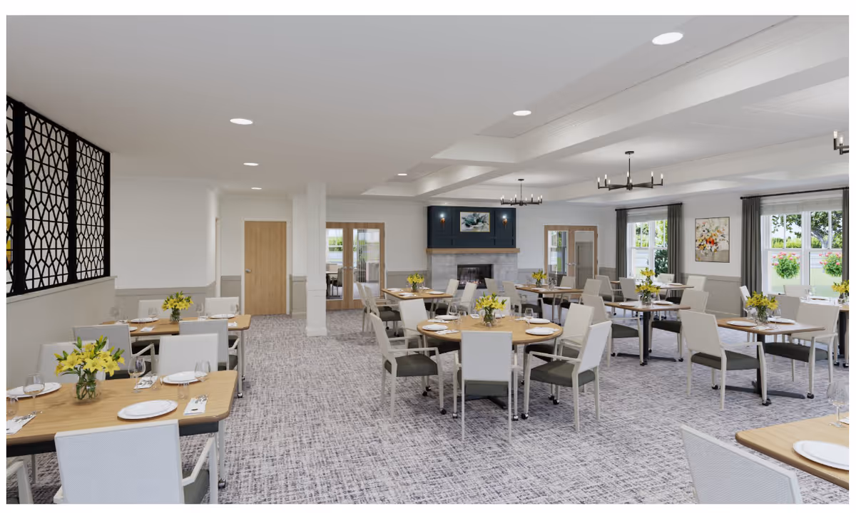 A spacious dining room in a senior living facility with multiple round and rectangular tables set with plates, glasses, and yellow floral centerpieces. The room features light-colored walls, large windows with gray curtains, a fireplace with a blue accent wall above it, and modern chandeliers hanging from the ceiling. There is a decorative black partition on the left side and double doors at the back leading to another room.