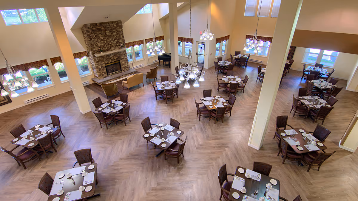 Spacious dining room with multiple set tables, chandeliers, and a stone fireplace, viewed from above.