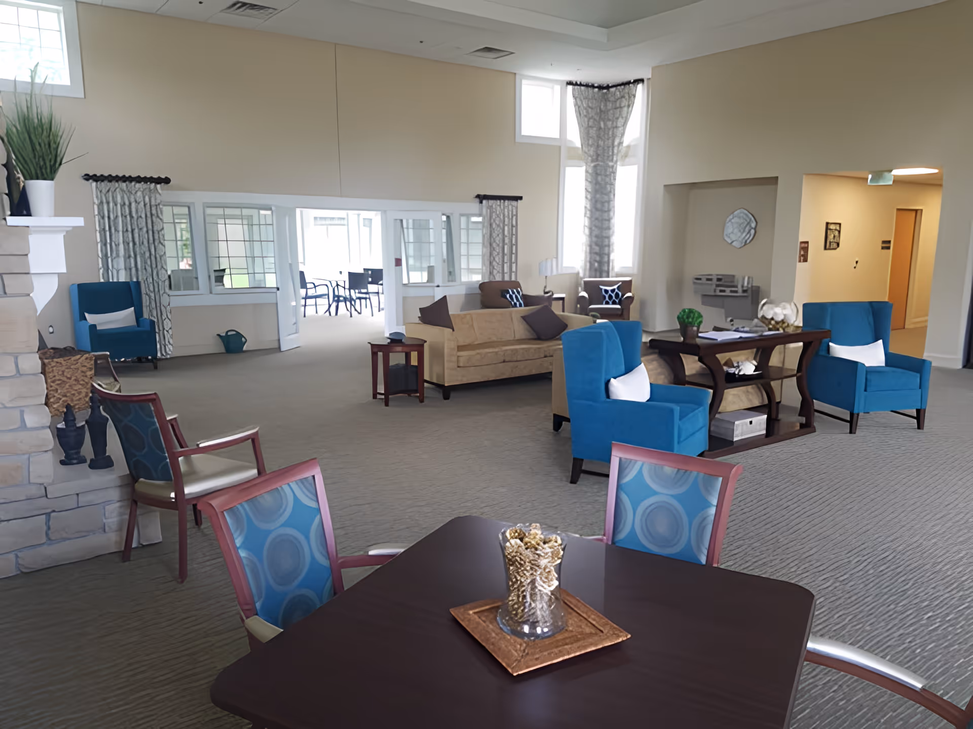Spacious furnished common lounge with sofas, armchairs, and tables under high ceilings and large windows.