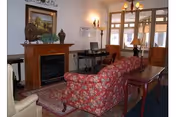 Communal living room with a patterned sofa and chairs facing a fireplace, a rug, a computer desk, and large windows/door.