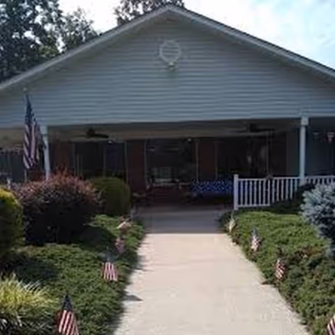 Front exterior of Ridge Rest Senior Living with walkway, garden beds, and American flags.