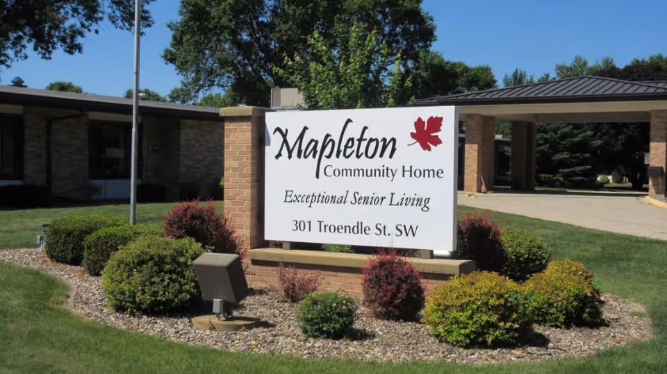 A white sign reading "Mapleton Community Home — Exceptional Senior Living — 301 Troendle St. SW" on a landscaped lawn in front of the facility.