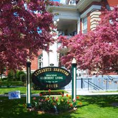 Exterior view of Elizabeth Brewster House with pink flowering trees and a sign.