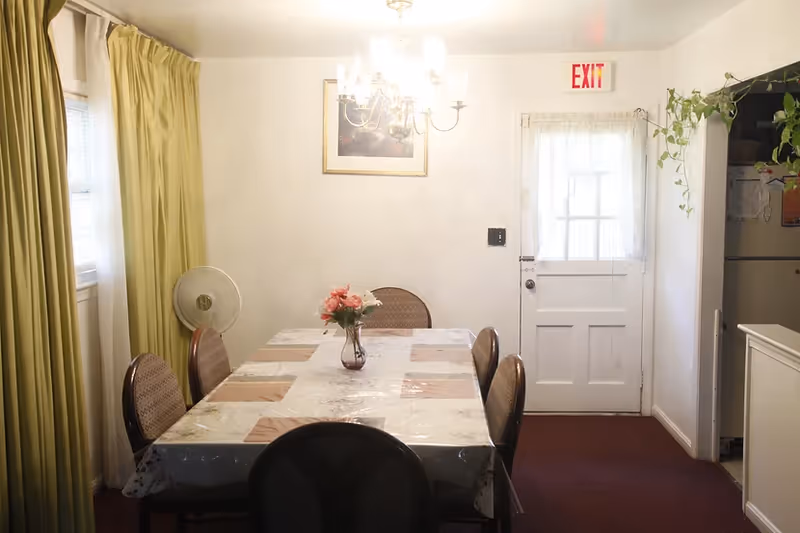 A dining room in a senior facility with a table, chairs, chandelier, and flowers.