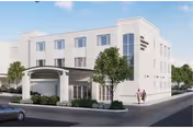 Three-story white senior living facility building with a covered entrance canopy, landscaping, and two people walking on the sidewalk.