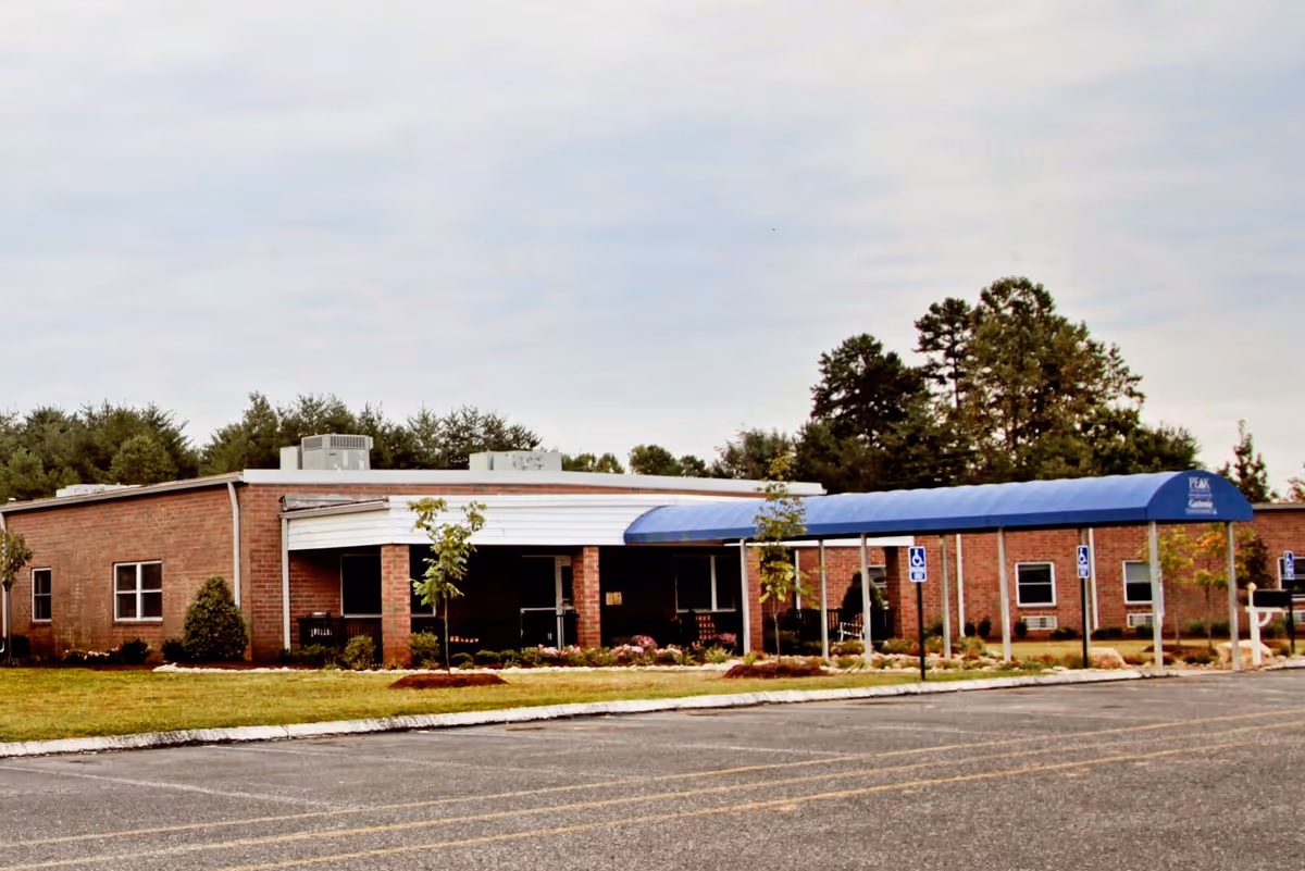 Front exterior of a single-story brick building with a blue covered entrance canopy and adjacent parking lot.