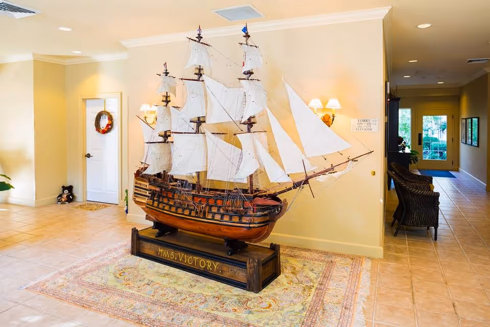 Large model sailing ship displayed on a stand in a bright lobby with tiled floors and seating in the background.