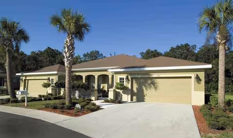 Exterior view of a single-story cream building with a two-car garage and palm trees.
