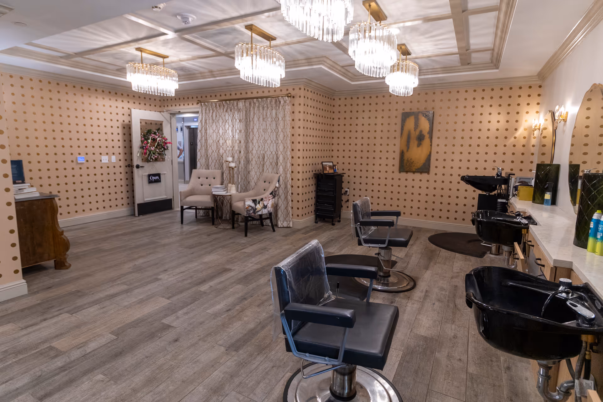 Well-lit interior hair salon with styling chairs, shampoo sinks, chandeliers and a small seating area.