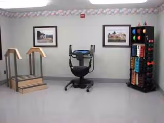 Indoor rehabilitation room with parallel bars, a central therapy chair, and an exercise bands rack.