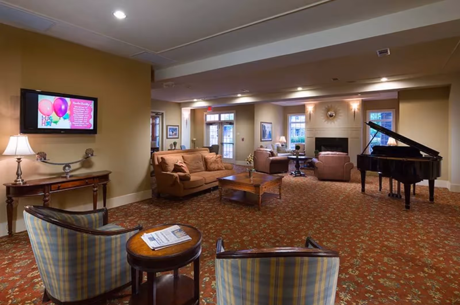 Spacious furnished common living room with sofas, armchairs, a grand piano, coffee tables and a wall-mounted TV.