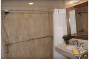 Tiled accessible bathroom featuring a walk-in shower with grab bars, shower curtain, sink, and mirror.