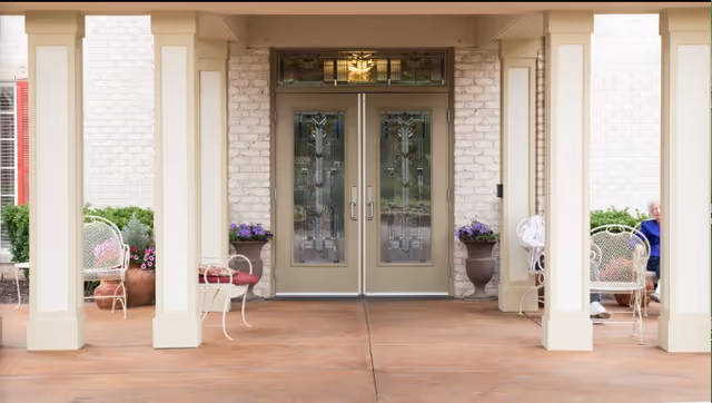 Glass double doors framed by stone walls and beige columns, with outdoor seating.