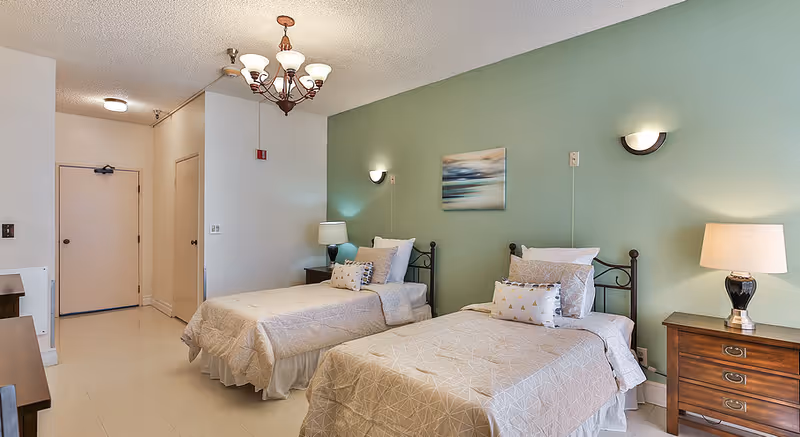 Two twin beds with matching quilts in a bright, hotel-style bedroom.