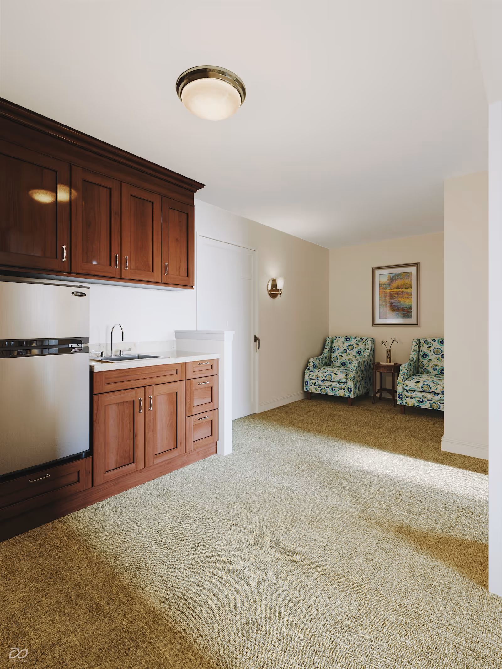 Sunlit senior living suite with a small kitchenette featuring wooden cabinets and a seating area with two patterned armchairs.
