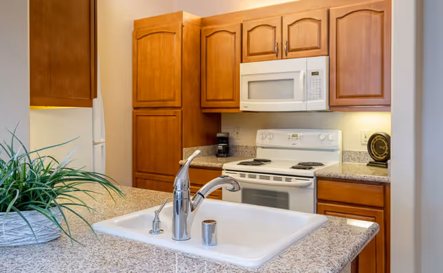 Kitchen with a granite island and sink in the foreground, white stove and microwave, and wooden cabinets in the background.