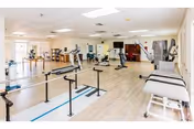 Spacious bright physical therapy/rehab room with parallel bars, treatment tables, and exercise equipment.