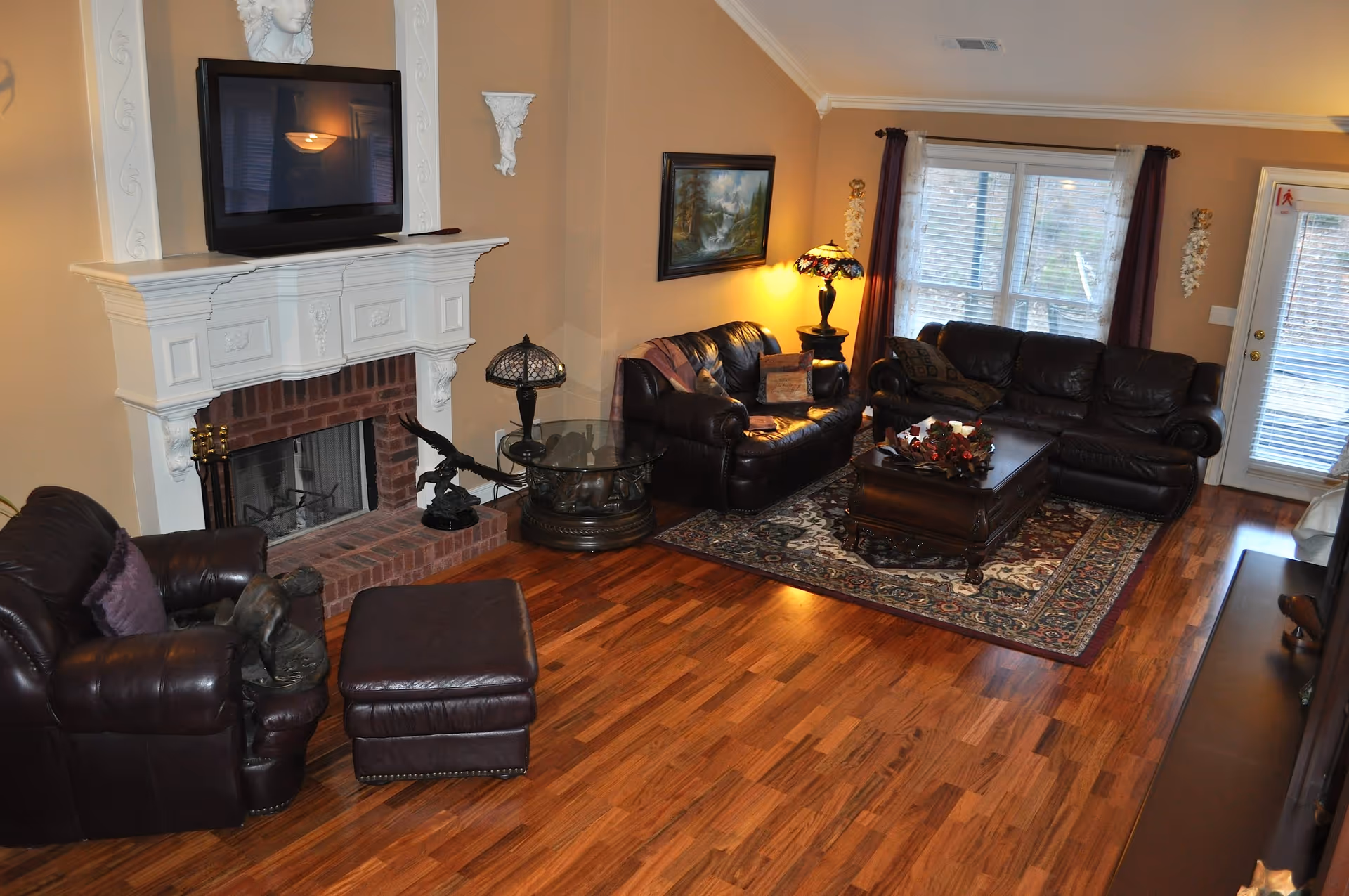 Spacious living room with leather sofas, a fireplace with a TV above, a coffee table on an area rug, and hardwood floors.