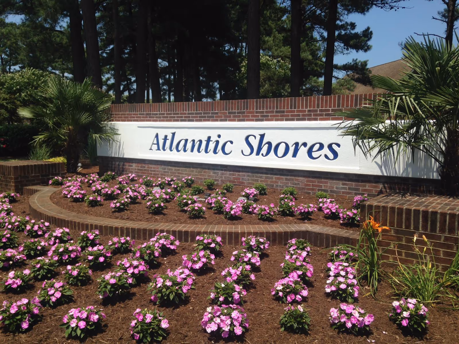 Entrance sign reading "Atlantic Shores" on a brick wall surrounded by landscaped flower beds and palm trees.