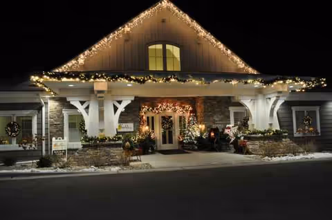 Nighttime exterior of Trouvaille Memory Care Suites with festive lights at the entrance.