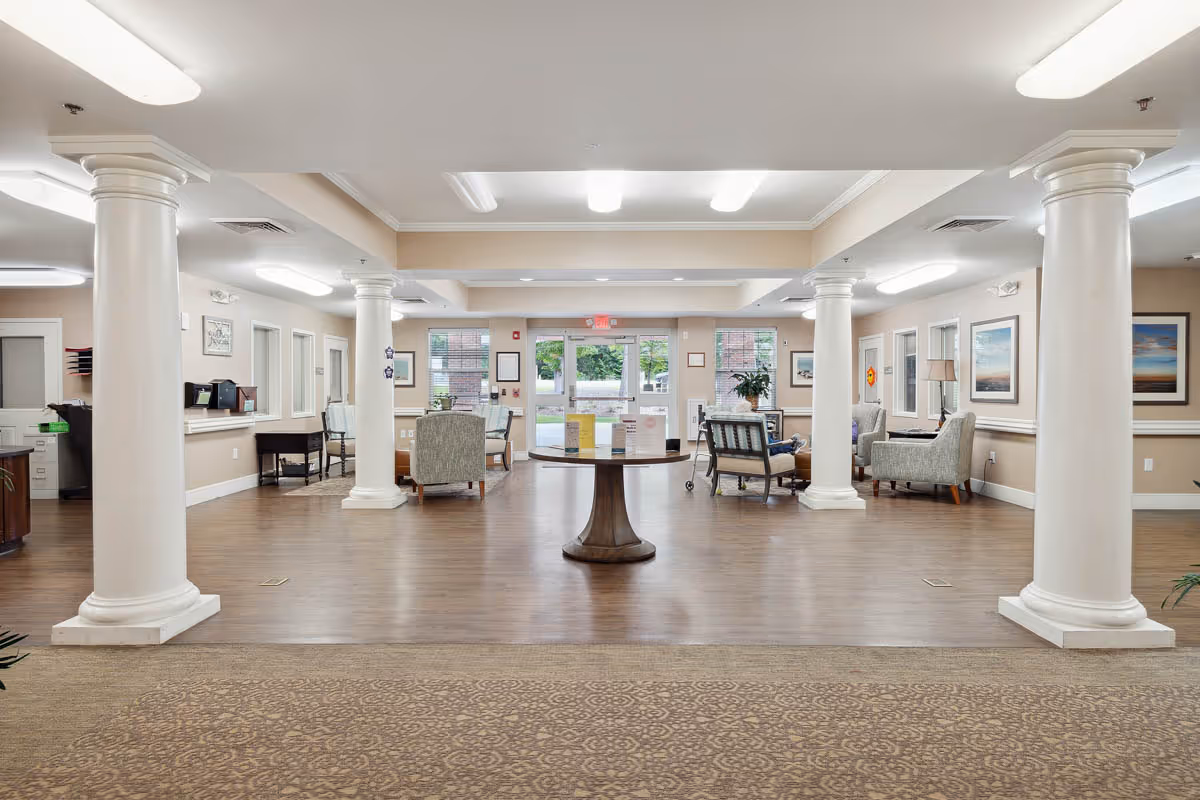 Spacious senior living lobby with white columns, seating areas, and a central round table.