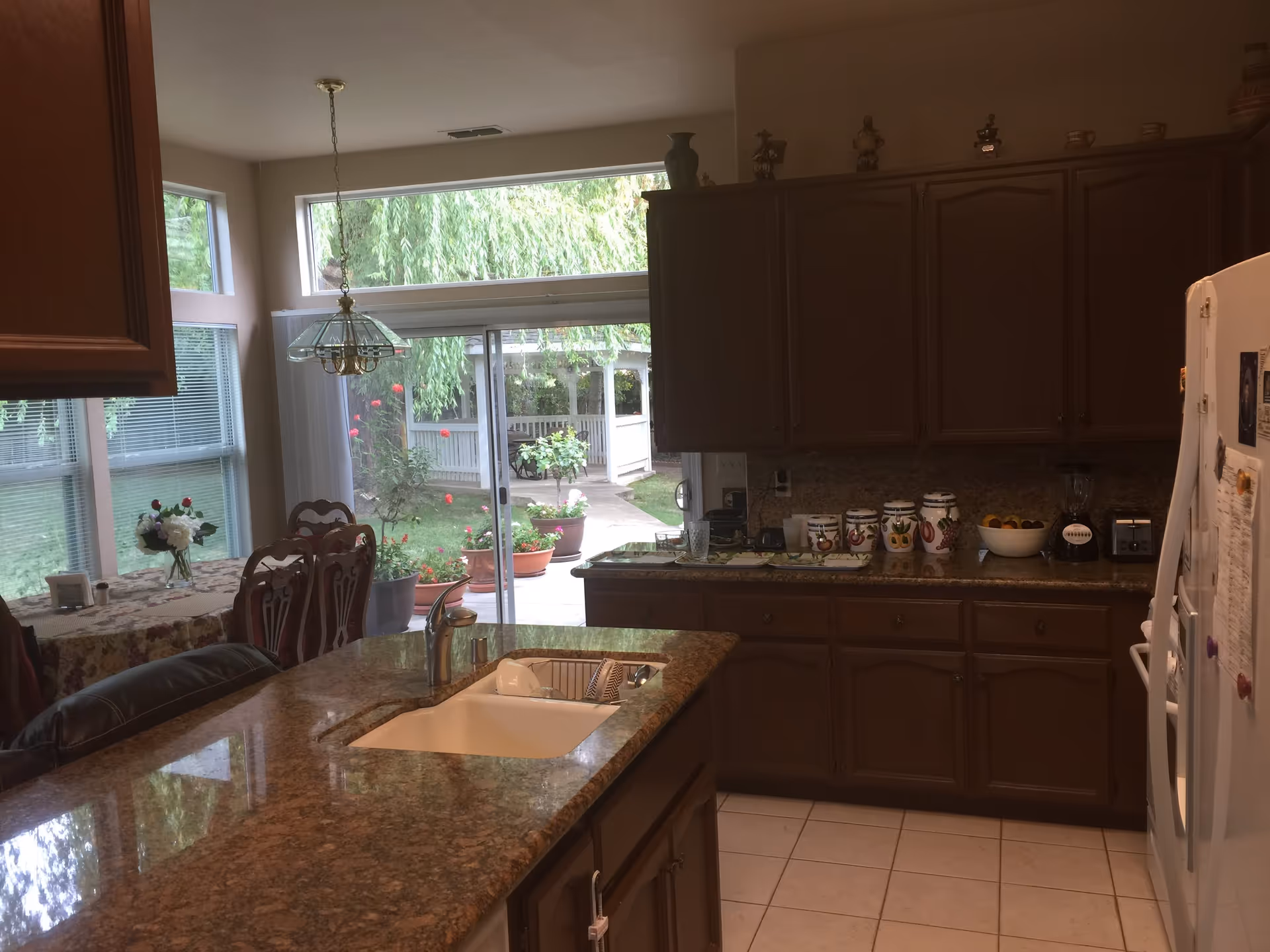 Kitchen interior with a granite island and sink, dark wood cabinets, a dining table by large windows, and a sliding glass door opening to a backyard.