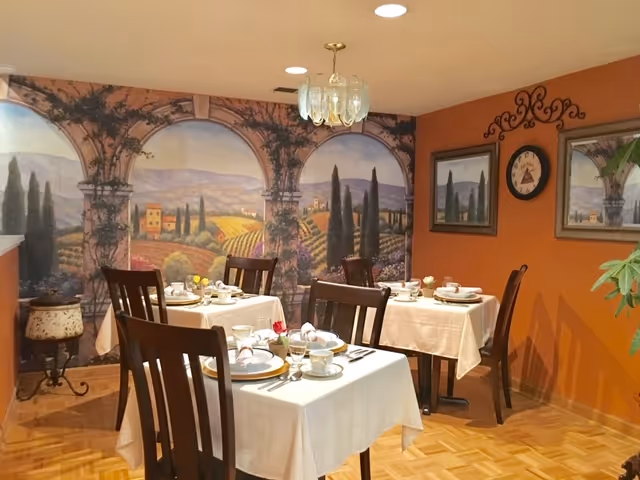 An interior dining room with white tablecloths, chairs, mural arches, and warm orange walls.