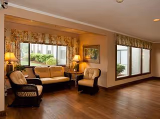 Cozy senior living living room with beige seating, lamps, and large windows.