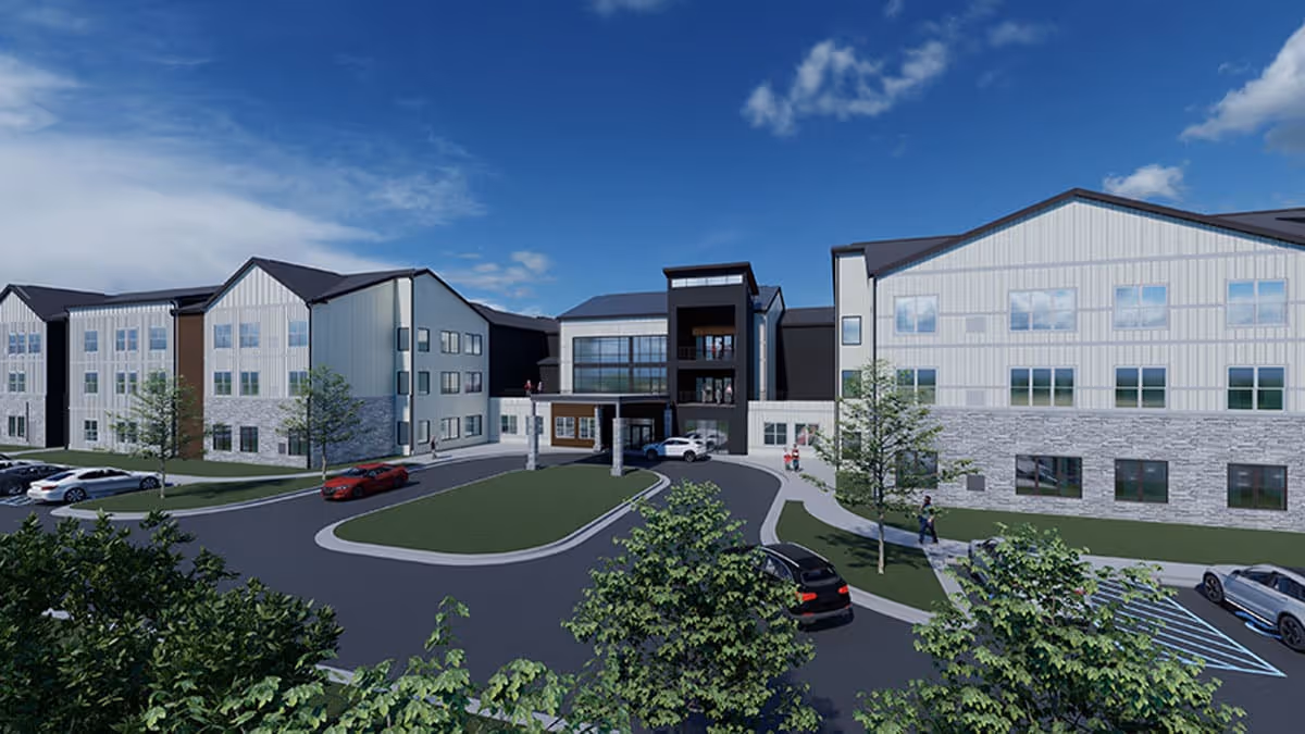 Exterior view of a modern senior living facility named Astral at Franklin, showing a three-story building with large windows, a covered entrance, a circular driveway, parked cars, trees, and a partly cloudy blue sky.