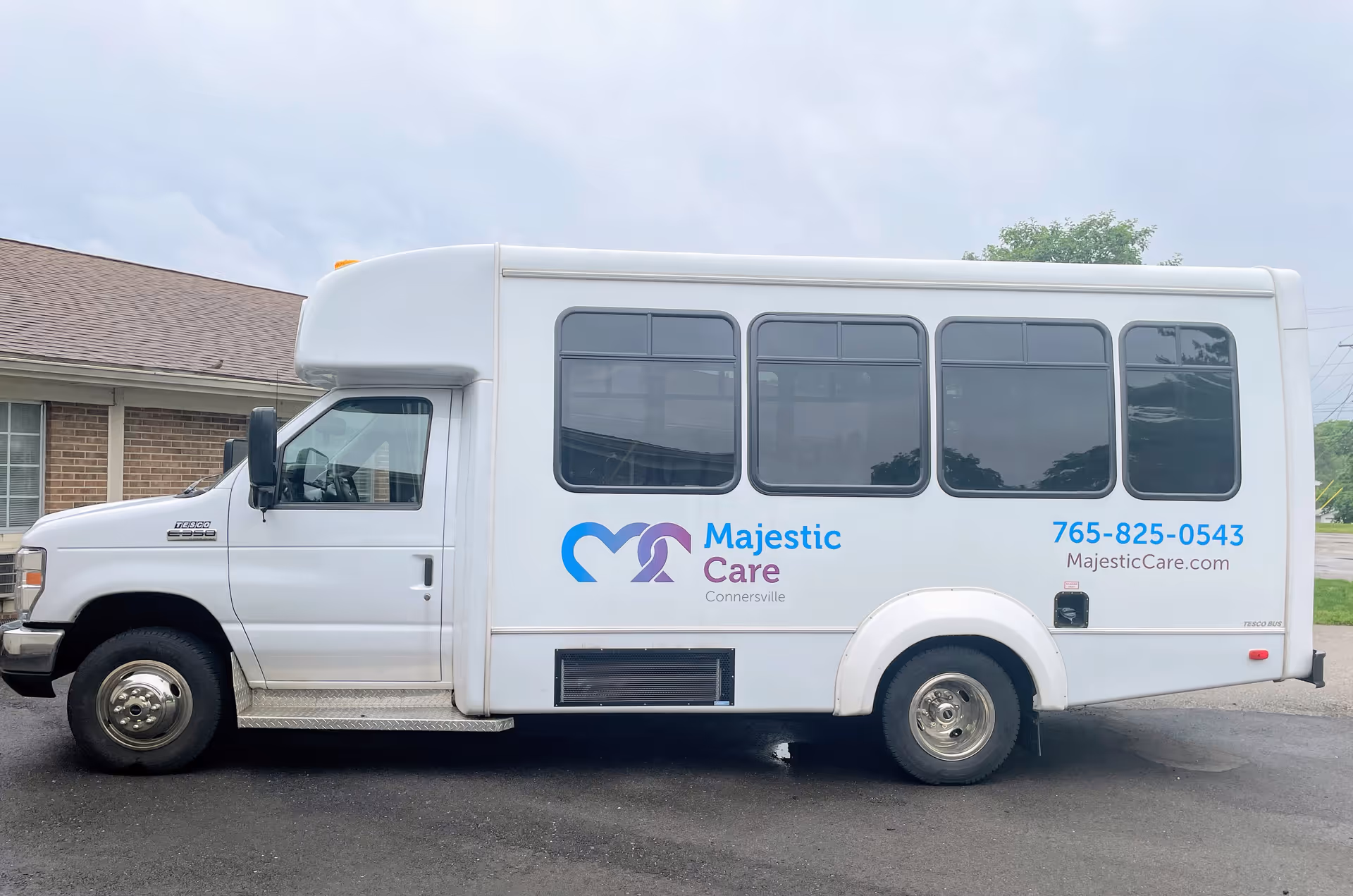 A white Majestic Care shuttle van parked outside a brick building with the facility logo and phone number on its side.