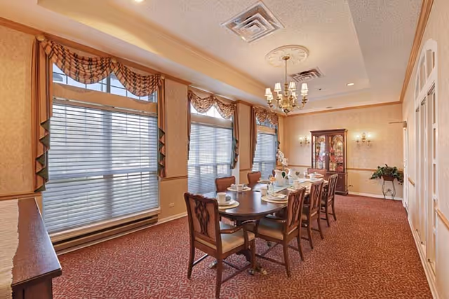 Formal dining room with a long wooden table set for a meal, upholstered chairs, large windows with valances, and a chandelier.