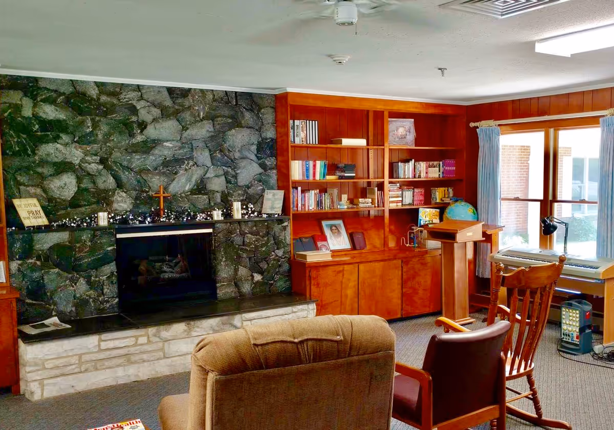 Cozy communal living room with a stone fireplace, built-in wooden bookshelves, seating, and a window letting in natural light.