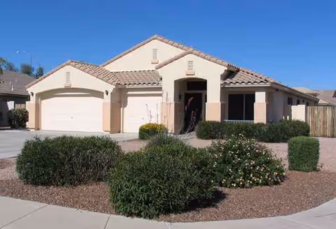 Single-story beige-assisted living facility with a tiled roof, front entrance, and desert landscaping.