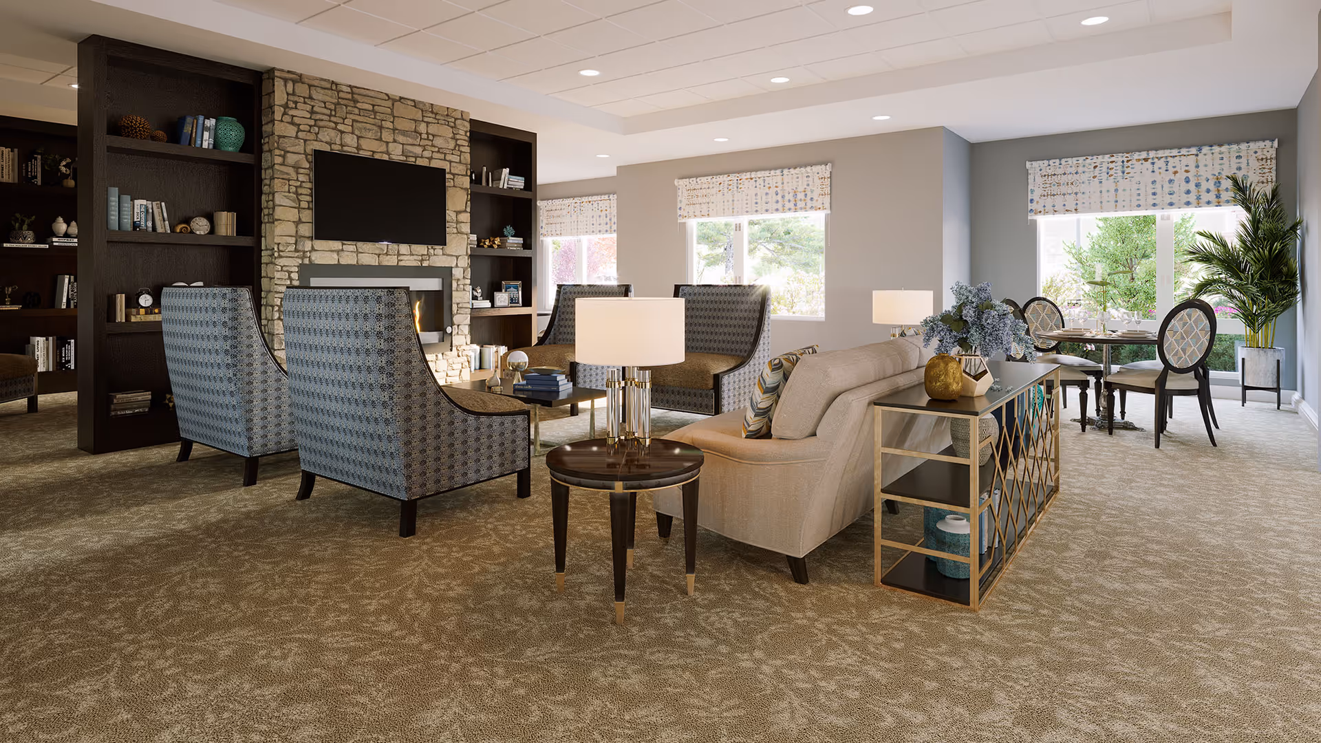 Spacious, well-lit senior living common room with comfortable seating, a stone fireplace and TV, bookshelves, and a dining area by the windows.