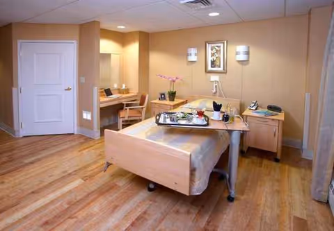 Senior living facility bedroom with adjustable bed, desk, and warm decor.