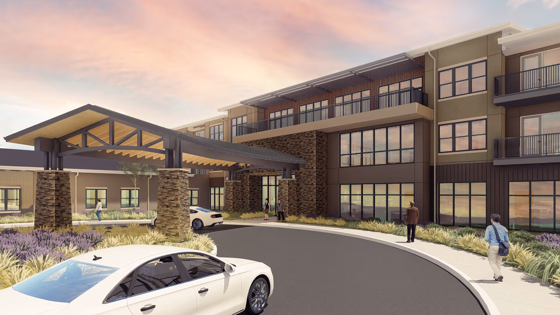 Exterior view of a modern senior living facility named Hillcrest Highlands of Gretna during sunset, featuring a covered entrance with stone pillars, landscaped greenery, a curved driveway with parked cars, and several people walking near the building.